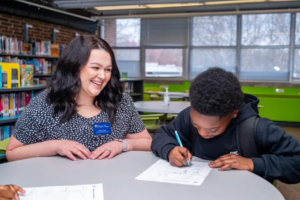 Graduate student sits and works with middle grades student to provide tutoring services.