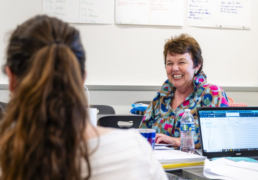 Teacher sits with student in classroom.
