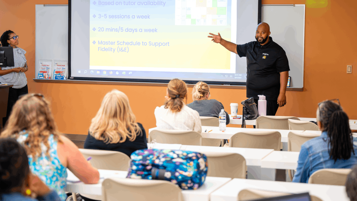Education practitioners and teachers sit in classroom listening to presenter during professional development session.